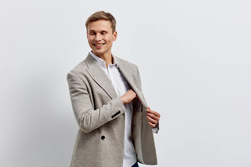 Smiling man in gray checkered blazer and white shirt pose confidently on plain light gray background studio shot. People lifestyle concept, casual style, fashion, success, positive energy, cheerful ex