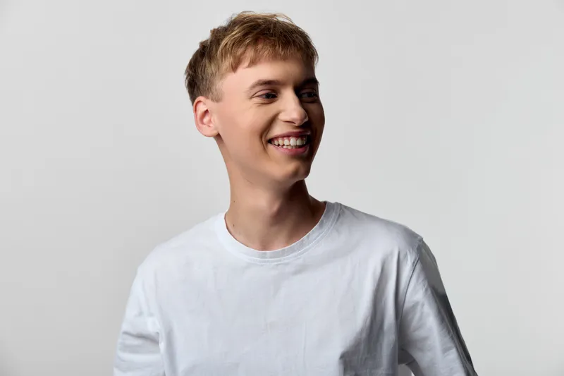 Smiling man wearing a white t shirt stands in a clean studio, emitting a casual confident vibe ideal for lifestyle, fashion, or advertising projects, with natural light and a relaxed appeal.