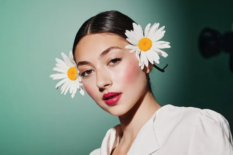 Beautiful young woman with floral hair accessories and glossy red lips poses fashionably against a soft green background. Concept of beauty, creative, and fashion.