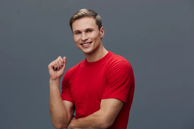 Smiling man wearing a bright red t-shirt look at camera cheerful positive casual pose isolated on gray background studio portrait. People lifestyle concept