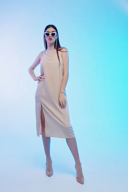 Tall woman in a beige dress and sunglasses poses confidently against a blue gradient background. The image highlights beauty, fashion, and elegance with modern styling and attitude.