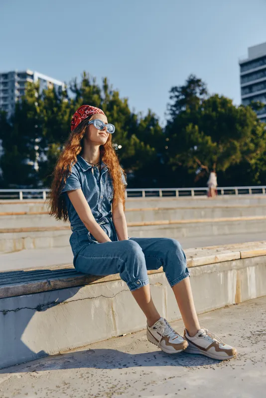 lifestyle woman in modern boho-western denim street style wearing sunglasses and red bandana, relaxed outdoors under bright natural light with film color tone