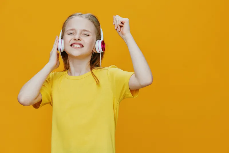 Happy child enjoying music with headphones on a vibrant yellow background, celebrating moments of joy and youthful energy