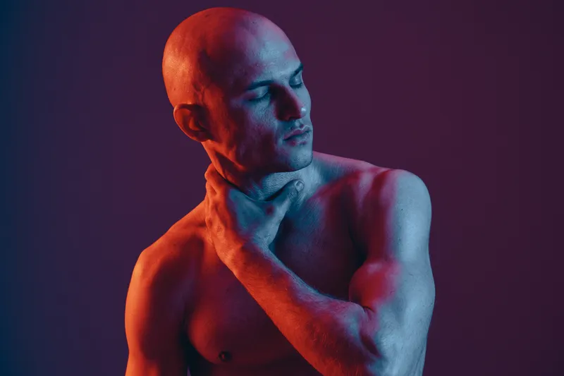 Artistic portrait of a man with dramatic lighting, showcasing muscle definition and emotional expression in a striking color palette.