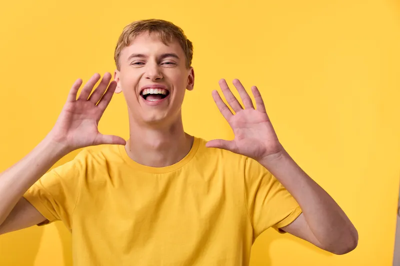 Happy male in a yellow shirt against a bright yellow background, energetic and smiling with raised hands, casual studio mood for lifestyle or advertising campaigns
