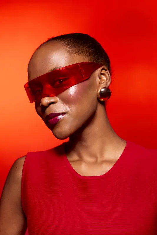 Portrait of an African woman with dark skin wearing red futuristic sunglasses and red top against an orange background. Concept of fashion, style, and modern beauty.