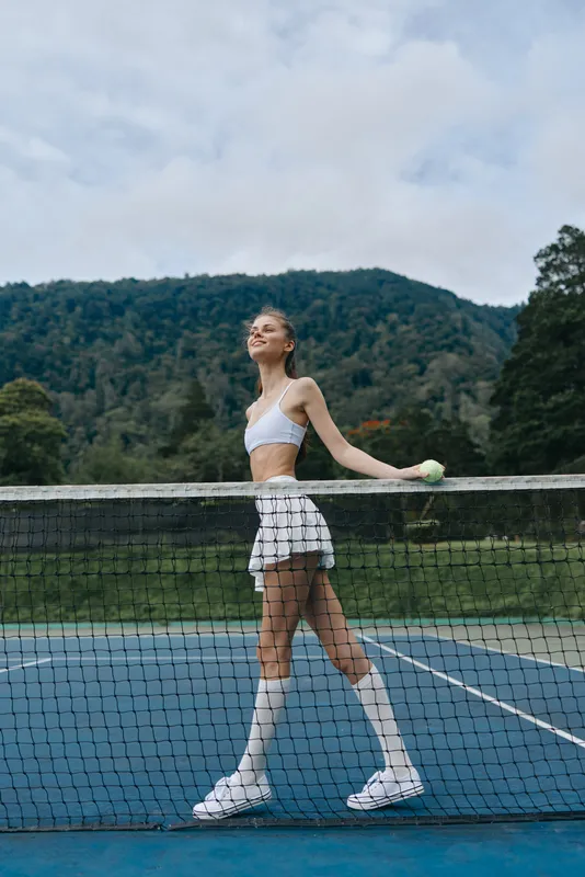 Young athletic woman in white tennis outfit enjoying a summer day on the court with a tennis ball, conveying joy and enthusiasm for sports