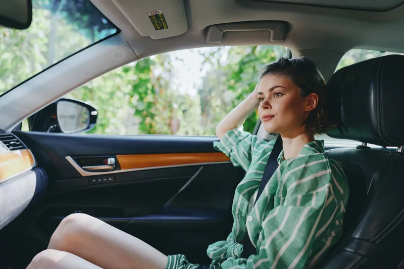 A relaxed woman sits in a car seat with a seatbelt fastened, looking out the window during a calm drive.