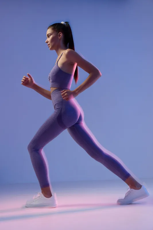 athletic woman exercising in purple sportswear stretching leg indoors with focused expression in studio light, showcasing fitness and active lifestyle.