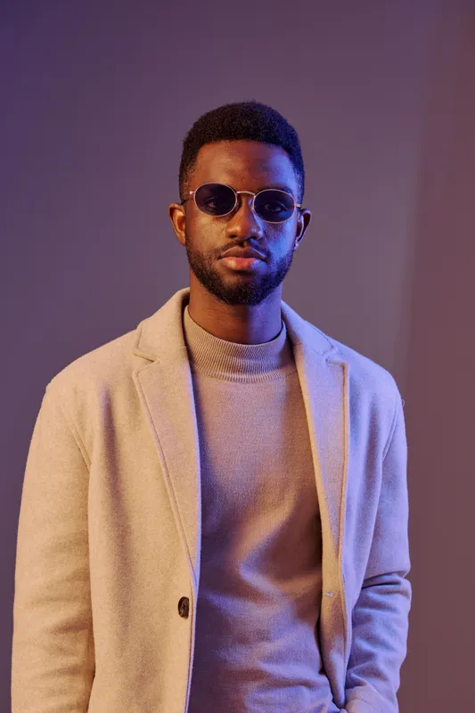 Stylish young African man in sunglasses and a sweater, posing confidently in a modern setting with a colorful background Fashion, confidence, and urban style