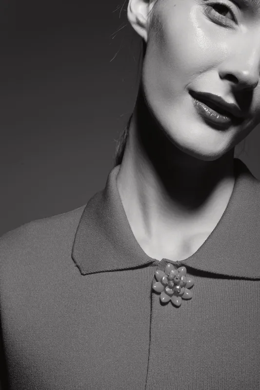 Close-up of a smiling white woman with light skin wearing a textured shirt and decorative brooch in a monochrome studio portrait. Concept of elegance, fashion, and beauty.