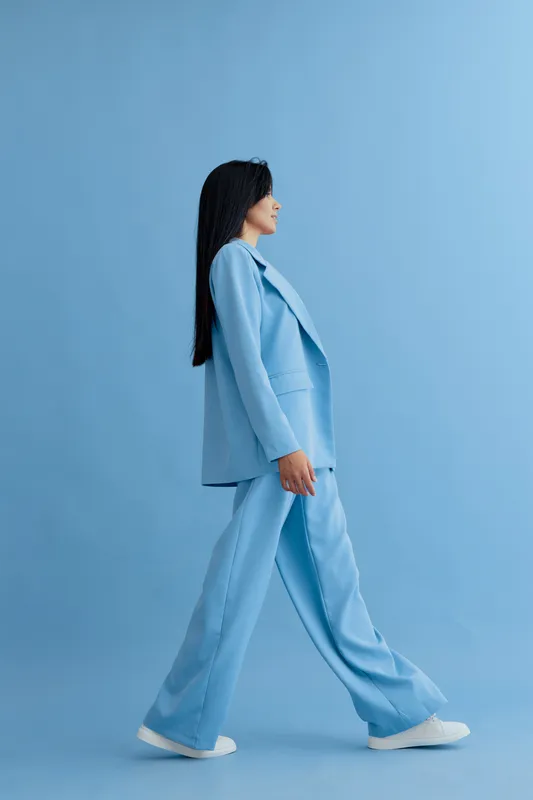 woman walking in blue suit with white sneakers on blue background, long dark hair and casual modern style, full length side profile portrait