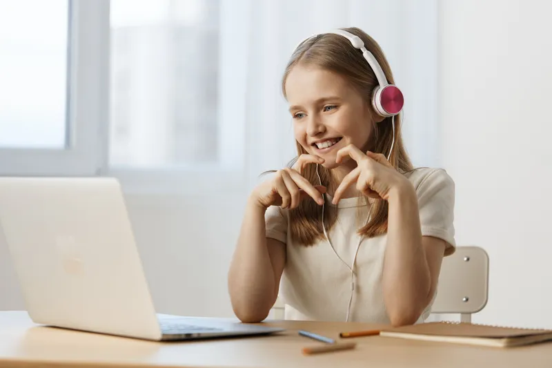 Young girl smiling while using a laptop, wearing headphones, in a bright and modern room, conveying joy and engagement with technology