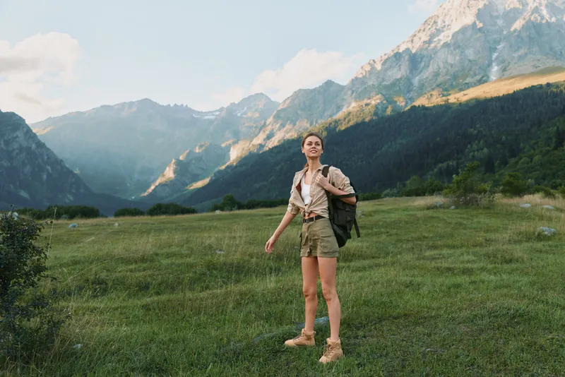 A young woman hikes through a mountain valley, feeling a sense of exploration and freedom as the landscape unfolds around her.