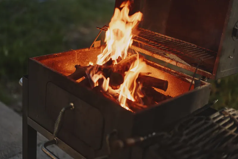 Bright flames dancing in a charcoal grill, showcasing cooking preparation for an outdoor barbecue, evoking a warm and inviting atmosphere of summer gatherings