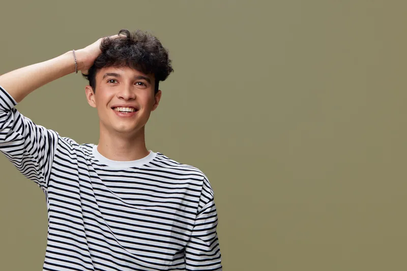 smiling man in striped shirt with curly hair posing against green background, casual style, happy expression, relaxed posture, youthful appearance, studio portrait
