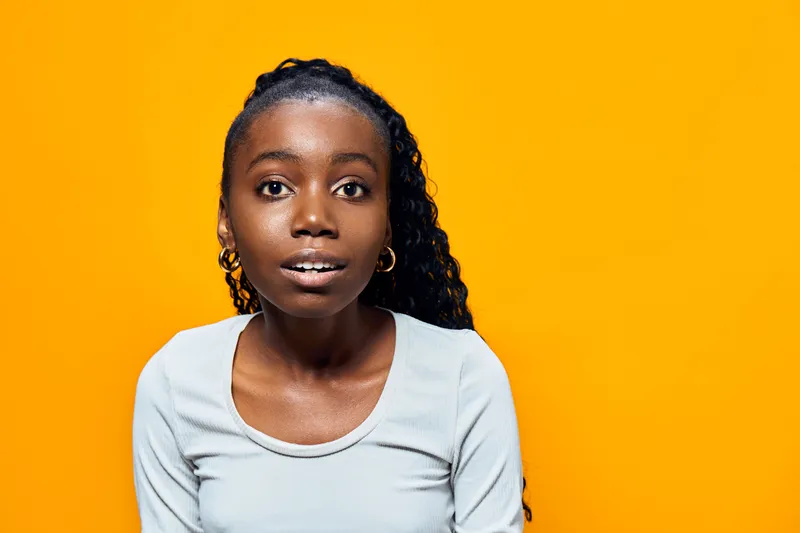 Young Black woman with curly hair smiling against a bright yellow background, showcasing joy and confidence in casual grey attire