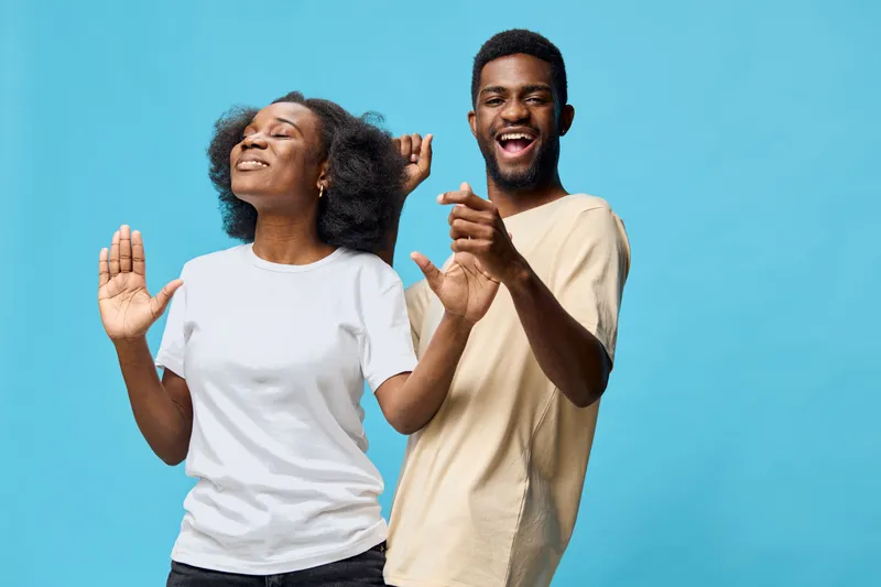 Happy young adults dancing together against a vibrant blue background, expressing joy and celebration with casual outfits in a bright and uplifting atmosphere