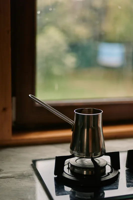 A gooseneck kettle rests on a gas burner in a home kitchen, metal shine and warm light create a cozy cooking scene.