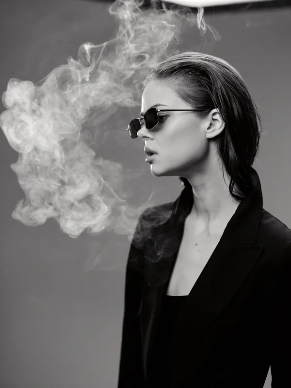 Black and white portrait of a stylish woman wearing sunglasses with smoke around her face