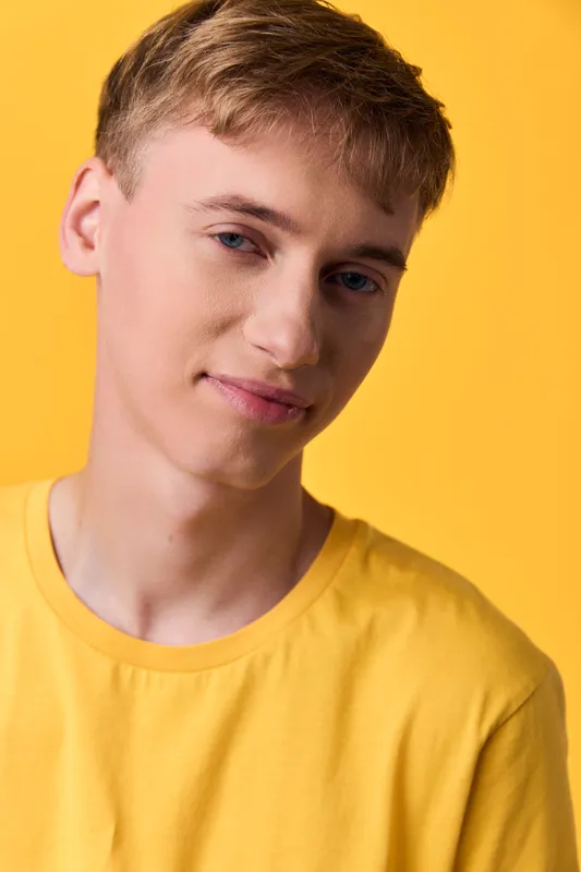 Young man in a bright yellow shirt against a yellow backdrop, relaxed pose, soft studio lighting, casual fashion, friendly expression, clean composition for lifestyle or fashion use