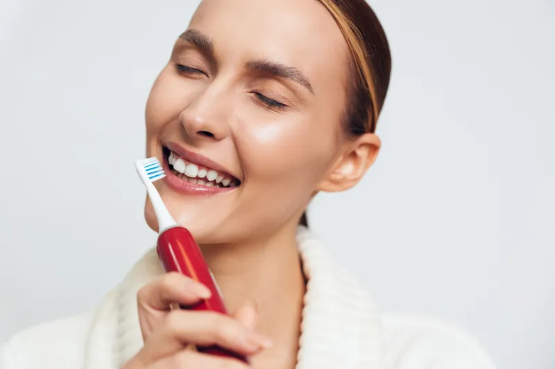 Smiling woman brushing teeth with toothbrush and toothpaste on white background, close up portrait, bright natural light, fresh hygiene moment, clean dental care routine today