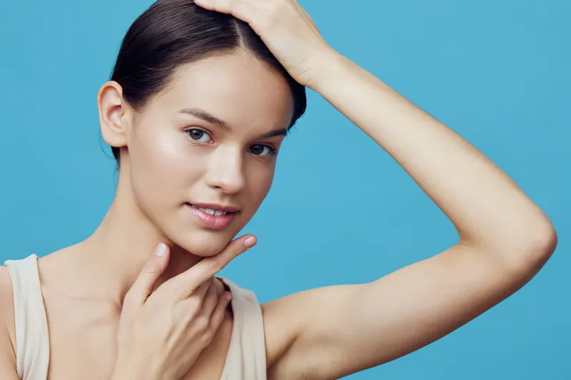 Young woman with a gentle smile posing against a turquoise background, showcasing healthy skin and natural beauty for skincare concepts