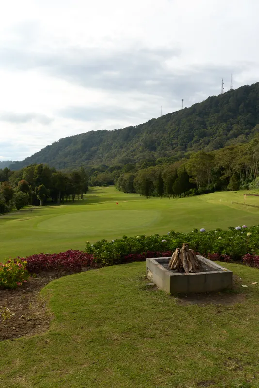 Scenic view of a golf course surrounded by lush greenery and mountains, featuring a fire pit in the foreground, perfect for outdoor relaxation and recreation
