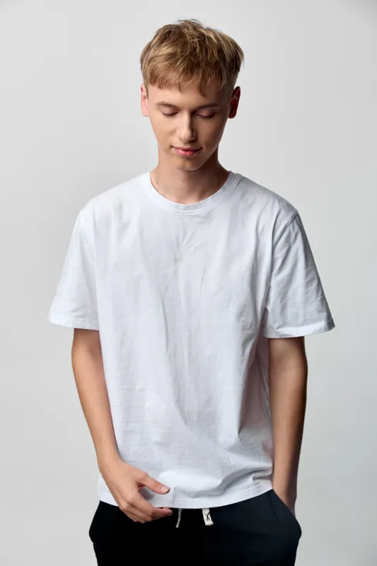 Teen boy in a casual white t shirt posing in a studio with relaxed expression, minimalist background, clean lines, modern fashion, everyday wardrobe for youthful style and ease