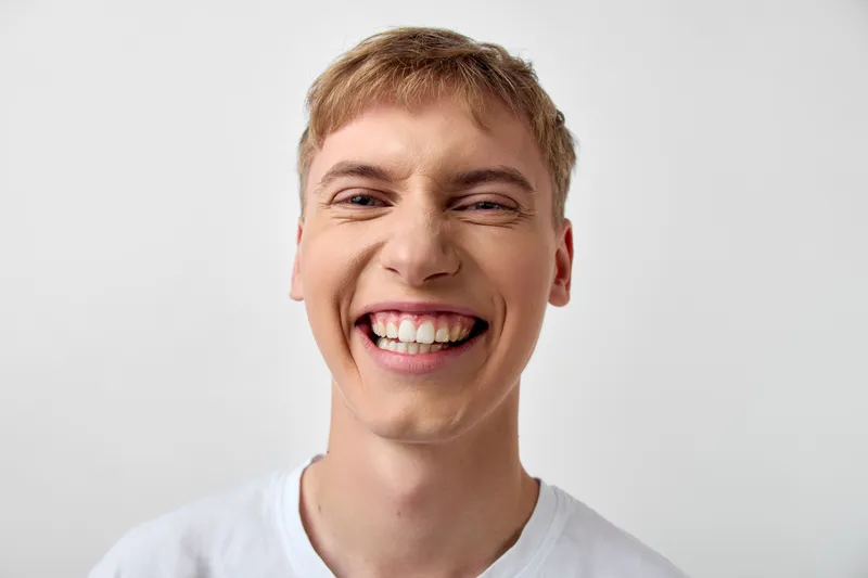 Smiling young man with bright teeth wearing a white t shirt, cheerful expression and warm mood, closeup view ideal for lifestyle, happiness, confidence, and positive energy in marketing visuals