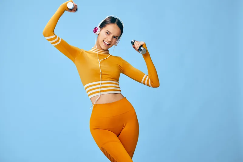 Woman fitness sport and workout with dumbbells in orange activewear, energetic studio scene, confident athlete performing cardio moves against blue background for lifestyle, health and motivation.
