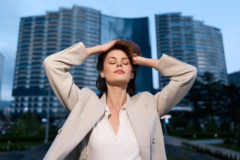 Confident woman in business attire enjoying success outdoors with modern architecture in the background, expressing empowerment and ambition.