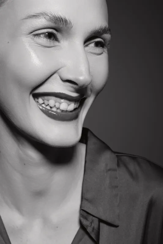 Close-up portrait of a smiling white woman with light skin and dark lipstick in black and white. Concept of happiness, beauty, and natural expression in studio lighting.