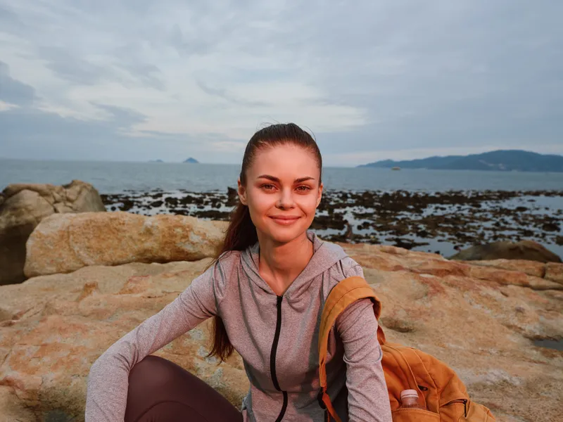 Smiling young woman in sportswear, enjoying the seaside view during sunset, embodying fitness and wellness, perfect for health and lifestyle concepts
