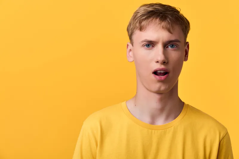 Man wearing a yellow t shirt with a surprised expression against a solid yellow background, studio lighting, casual mood, expressive face, vibrant and modern stock image for branding