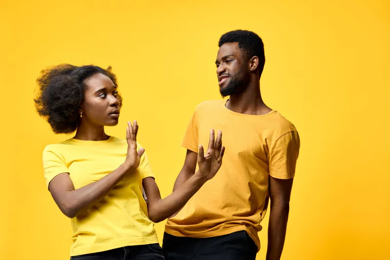 Young African couple in matching yellow shirts experiencing playful disagreement against a bright yellow background, showcasing emotion and vibrant energy