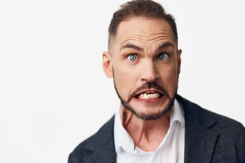 A business professional man on a colored isolated background, displaying intense emotion with raised eyebrows and clenched teeth, ready for bold presentation and clear communication.