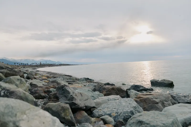 Rocky coastline with calm sea and cloudy sky during sunset. Soft natural light reflects on water surface. Concept of nature landscape, peaceful ocean, and outdoor scenery.