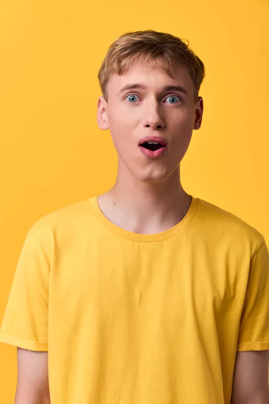 Surprised man in a yellow tee stands against a bright background, showcasing a spontaneous expression and curious mood, ideal for product reveals, upbeat campaigns and lifestyle promotions