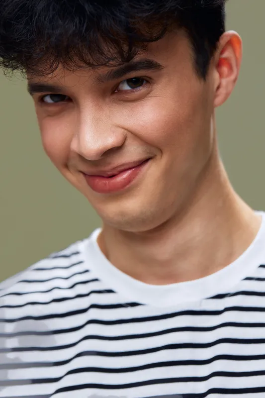 young man smiling wearing striped shirt with curly dark hair close-up portrait with soft green background, happy expression and natural lighting