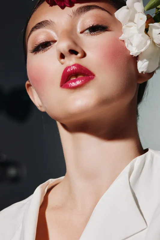 Close-up portrait of fashionable woman with red lips and natural floral accessories. Bright makeup and glowing skin, conceptual beauty creativ shot for fashion and editorial use.