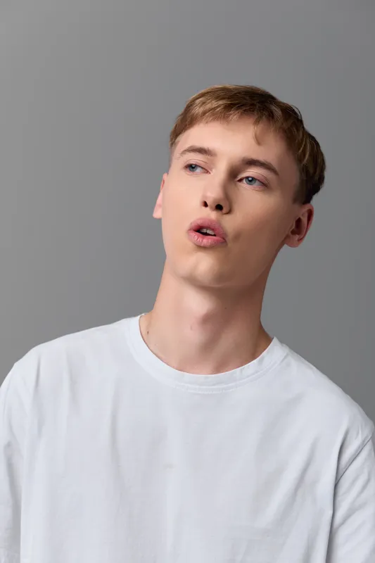 Young man in a white shirt speaks with an open mouth, captured in a studio close up, highlighting a candid expression and a moment of dialogue.
