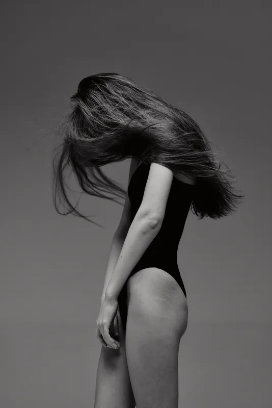 Black and white portrait of a woman with flowing hair in a bodysuit, minimalistic and elegant pose, artistic fashion concept.