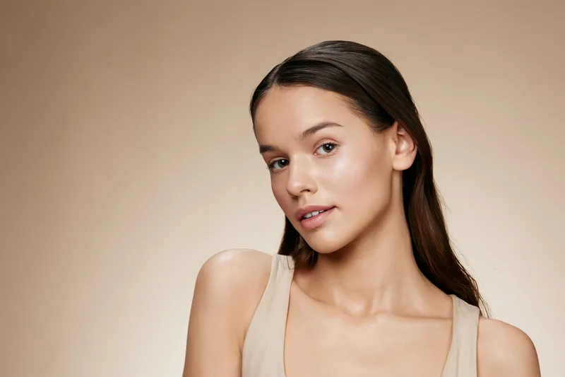Beautiful young model with flawless skin in neutral tones, exuding confidence against a soft beige background, ideal for beauty and skincare concepts