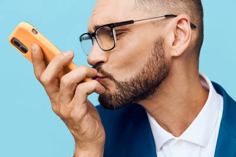 Professional businessman portrait with a focused mood, isolated on a vivid blue background. The subject conveys emotion and concentration while engaging with a mobile device.