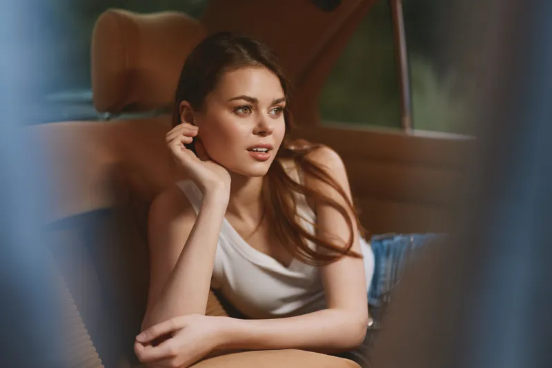 Young woman in casual attire relaxing in a car, showcasing an expressive smile and a laid-back pose, emphasizing comfort and leisure.