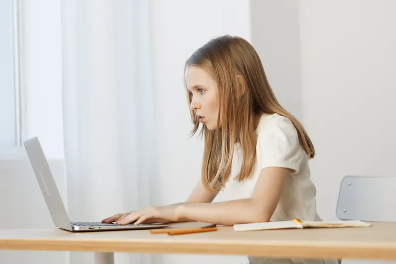 Focused girl working on a laptop in a bright, minimalistic room, representing concentration and productivity during study time