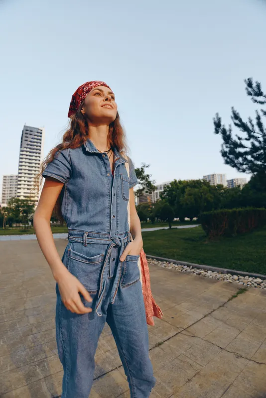 Lifestyle woman in modern boho-western denim street style standing outdoors with a confident expression, film color mood, casual urban atmosphere, summer lighting.