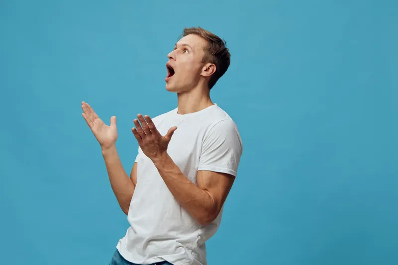 surprised young caucasian man wearing white t-shirt casual standing blue background emotional expression digital detox concept
