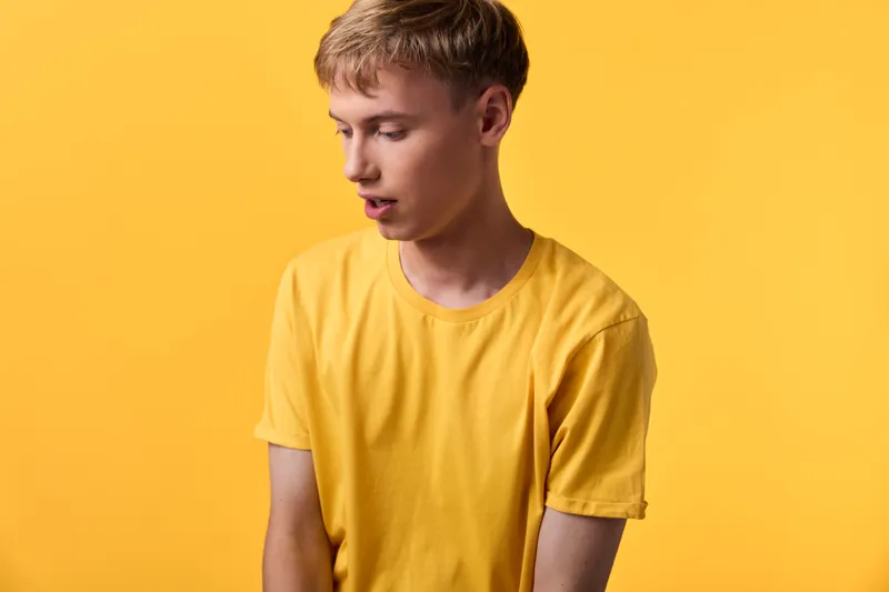 Man in a bright yellow shirt stands against a vivid studio backdrop, casual pose and subtle focus create a minimalist mood, warm tones and clean lines, contemporary fashion feel with no branding